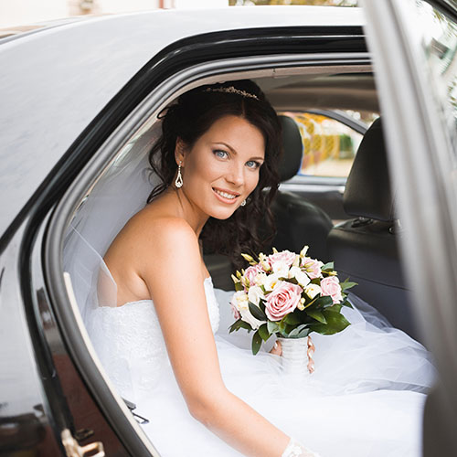 beautiful bride with flowers getting in a car